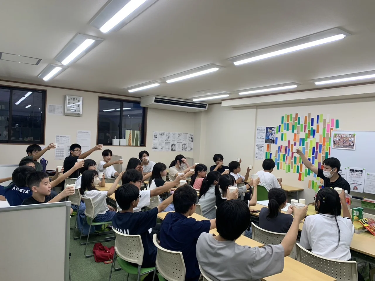 個個塾の教室で先生と生徒たちが紙コップを持って交流する様子