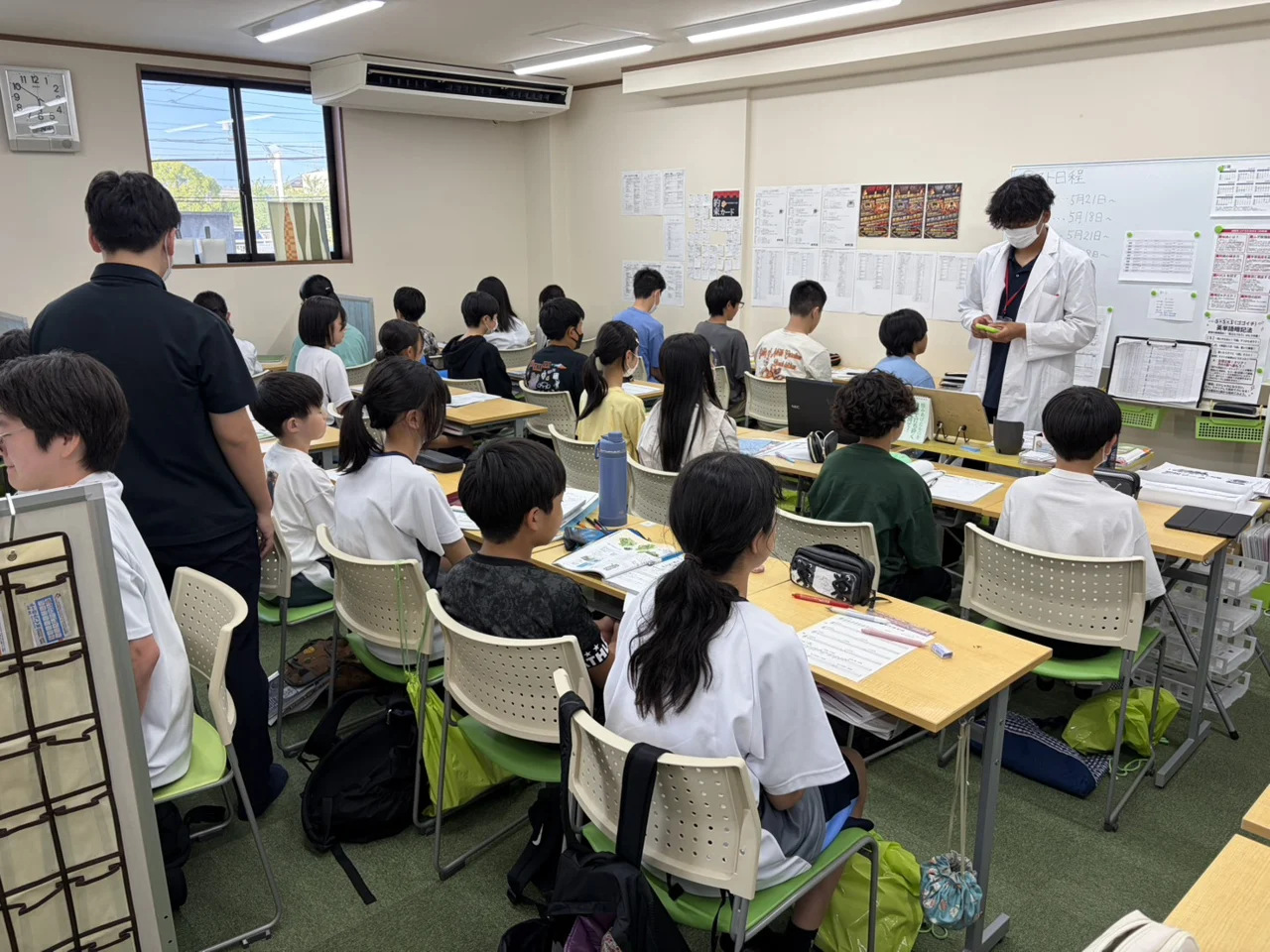 個個塾の教室で先生が生徒たちの学習のそばに立つ様子