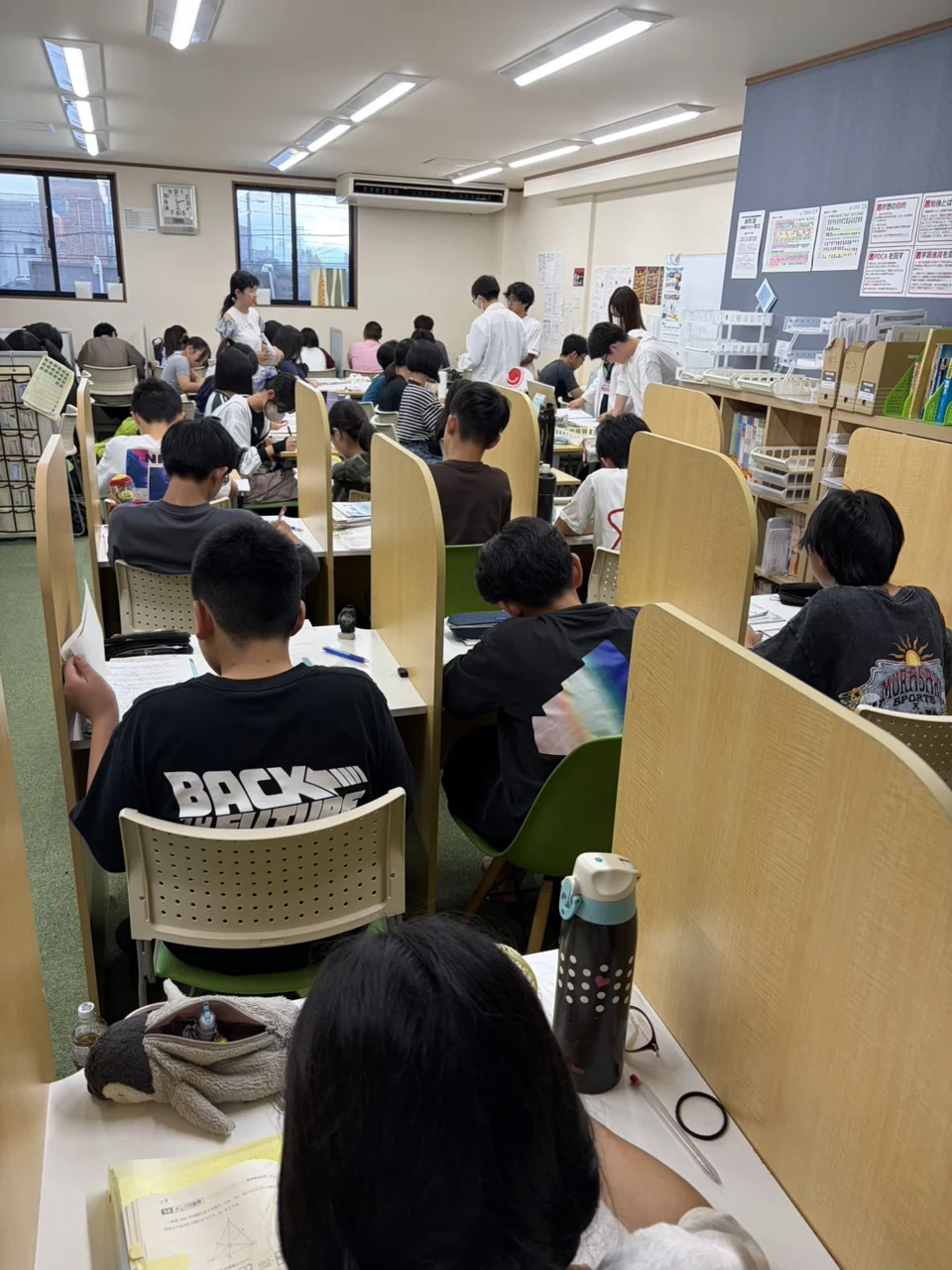 個個塾の教室で生徒が学習し、先生が机のそばで対応する様子